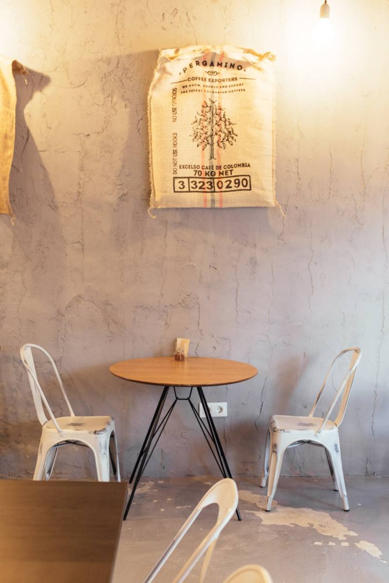 Mesilla y sillas en Cafetería BREW COFFEE con un saco café de 70kg vacio a modo de cuadro decorativo en pared