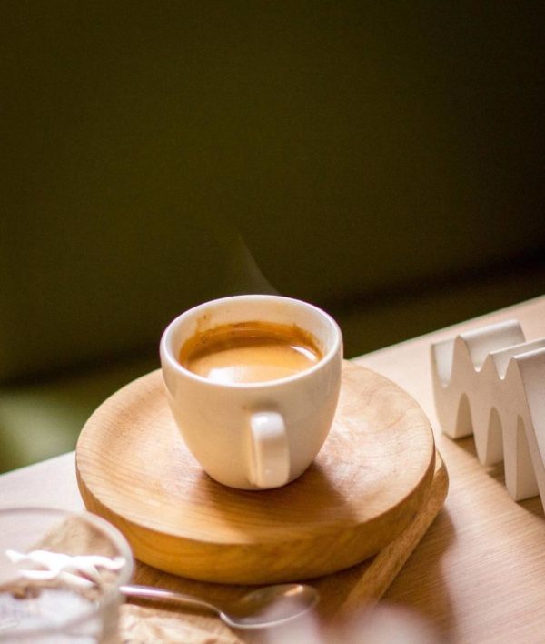 Tacita con café sólo humente sobre plato de madera preparado en la cafetería FRENESÍ CAFÉ de Barcelona.