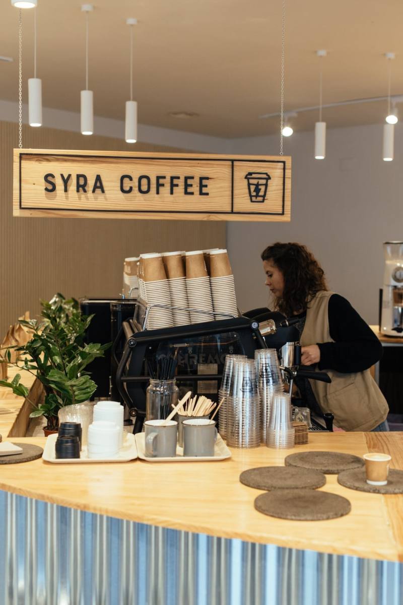 Chica manipula máquina de café en la cafetería SYRA COFFEE, visto desde la barra.